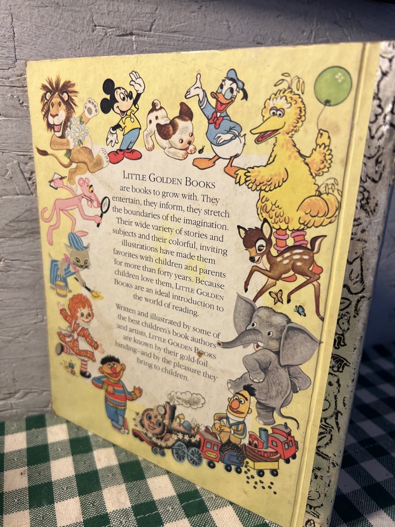 May include: A yellow book cover with the title "Little Golden Books" and a description of the books. The cover features illustrations of popular children's characters including Mickey Mouse, Donald Duck, Big Bird, and a pink panther.
