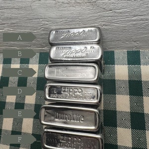 May include: A stack of six silver Zippo lighters. The lighters are stacked on top of each other, with the top lighter being a silver Zippo lighter with the word "Zippo" engraved on it. The second lighter from the top is a silver Zippo lighter with the word "Zippo" engraved on it. The third lighter from the top is a silver Zippo lighter with the word "Zippo" engraved on it. The fourth lighter from the top is a silver Zippo lighter with the word "Zippo" engraved on it. The fifth lighter from the top is a silver Zippo lighter with the word "DuroLite" engraved on it. The bottom lighter is a silver Zippo lighter with the word "Zippo" engraved on it.