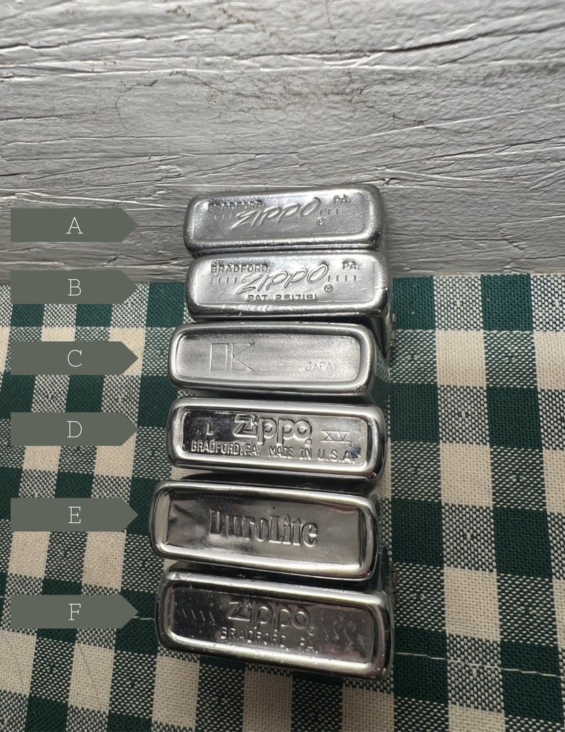 May include: A stack of six silver Zippo lighters. The lighters are stacked on top of each other, with the top lighter being a silver Zippo lighter with the word "Zippo" engraved on it. The second lighter from the top is a silver Zippo lighter with the word "Zippo" engraved on it. The third lighter from the top is a silver Zippo lighter with the word "Zippo" engraved on it. The fourth lighter from the top is a silver Zippo lighter with the word "Zippo" engraved on it. The fifth lighter from the top is a silver Zippo lighter with the word "DuroLite" engraved on it. The bottom lighter is a silver Zippo lighter with the word "Zippo" engraved on it.