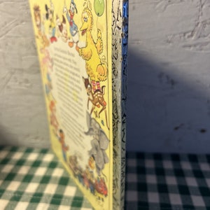 May include: A vintage children's book with a yellow cover featuring a variety of cartoon characters, including Mickey Mouse, Donald Duck, Big Bird, and a deer. The book's title is "The Sesame Street Book of First Words".