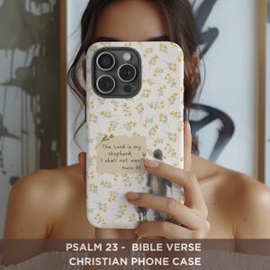 May include: A phone case with a floral pattern and the text "The Lord is my shepherd; I shall not want Psalm 23." The case also features a watercolor illustration of a person and a dog. The case is white with yellow flowers.