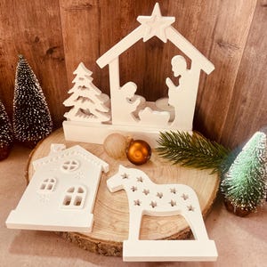 Könnte beinhalten: Weiße Weihnachtsdekorationen aus Holz, darunter eine Krippe, ein Haus und ein Schaukelpferd. Die Dekorationen sind unvollendet und bereit zum Bemalen.