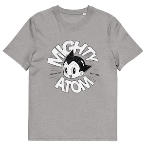 以下が含まれることがあります： グレーのTシャツ。白黒の漫画のキャラクター、Mighty Atomのグラフィックがプリントされています。「MIGHTY ATOM」の文字が円形に配置され、「TEZUKA INC.」と「EST. 1952」の文字も表示されています。