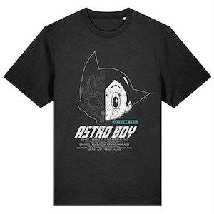 Peut inclure: Un t-shirt noir avec un graphique blanc du visage d'Astro Boy, un côté montrant ses parties robotiques et l'autre côté montrant son visage humain. Le texte "Tezuka Inc." et "Astro Boy" est imprimé sous le graphique. Le texte sous le graphique liste les spécifications d'Astro Boy.