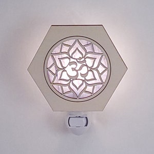 Könnte beinhalten: Weißes sechseckiges Nachtlicht mit einem ausgeschnittenen Design einer Lotusblume und dem Om-Symbol. Das Licht ist an und leuchtet.