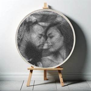 May include: A black and white string art portrait of two people with their heads close together. The artwork is framed in a white circle and is displayed on a wooden easel.