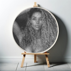 May include: A black and white portrait of a person's face created with string art. The art is displayed on a round wooden frame and is mounted on a wooden easel.