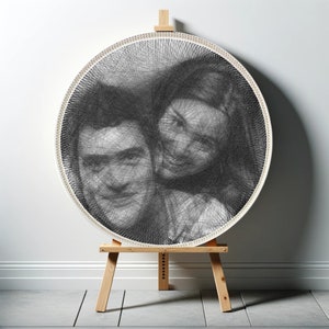 Puede incluir: Un marco circular blanco con un retrato de pareja en arte de hilo negro y blanco. El marco está en un caballete de madera.