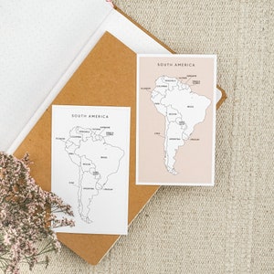 May include: Two black and white outline maps of South America on white paper with the names of each country labeled. The map on the left is on a brown surface and the map on the right is on a pink surface.