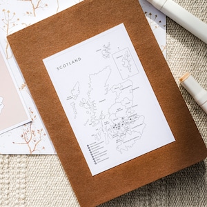 May include: A black and white map of Scotland with the regions labeled. The map is printed on a white sheet of paper and is sitting on a brown leather notebook.
