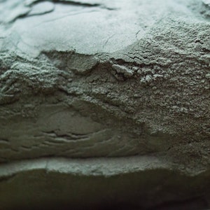 Könnte beinhalten: Nahaufnahme eines Haufens dunkelgrauen Pulvers. Das Pulver hat eine raue, strukturierte Oberfläche.