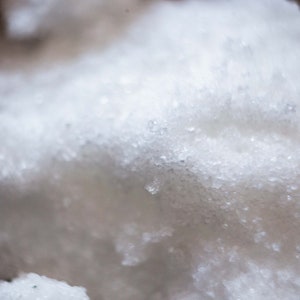 以下が含まれることがあります： 雪や砂糖のような、白くてふわふわした物質のクローズアップ。質感はざらざらしていて、小さな個別の結晶でできているように見えます。