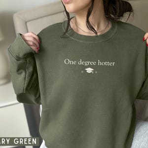 Pu&ograve; includere: Felpa verde militare con la scritta "One degree hotter" e una grafica del cappello di laurea. Il top a girocollo a maniche lunghe &egrave; realizzato in materiale morbido.