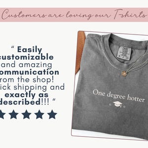 Pu&ograve; includere: Una maglietta grigia con la scritta "One degree hotter" e una grafica di cappello di laurea. La maglietta ha un girocollo e maniche corte. Una collana con pendente dorato &egrave; sulla maglietta. L'immagine include anche recensioni dei clienti.
