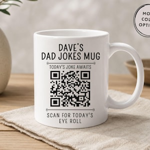 May include: A white ceramic mug featuring black text that reads DAVE'S DAD JOKES MUG, TODAY'S JOKE AWAITS, and SCAN FOR TODAY'S EYE ROLL, centered around a large black and white QR code. A circular badge in the top right corner says MORE COLOR OPTIONS.