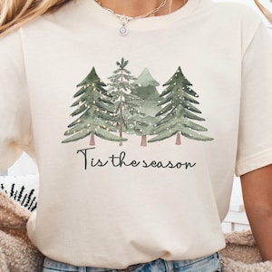 cream Bella Canvas® shirt with watercolor Christmas trees and text “Tis the season”, festive holiday tee with Canva-style design