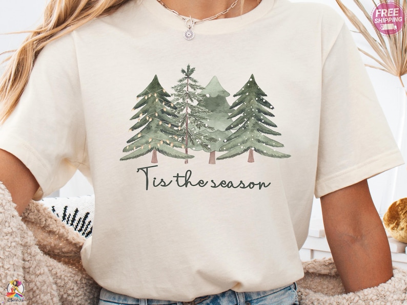 cream Bella Canvas® shirt with watercolor Christmas trees and text “Tis the season”, festive holiday tee with Canva-style design