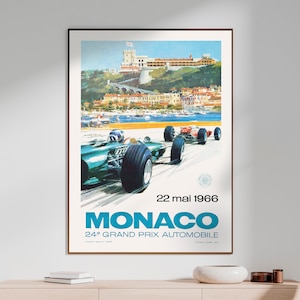 May include: Vintage poster for the 24th Monaco Grand Prix Automobile, held on May 22, 1966. The poster features a green race car speeding through a turn, with the city of Monaco and the Mediterranean Sea in the background.