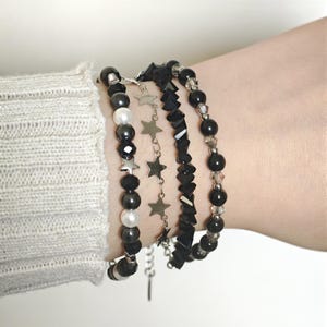 May include: A set of four bracelets featuring black round beads, white round beads, and a silver-toned chain with small star-shaped charms. One bracelet consists of faceted black beads, while another features alternating black and white beads.