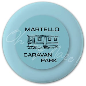 May include: A light blue round disc with a black and white illustration of a mobile home and the text "Martello Caravan Park".