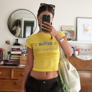 May include: A yellow cropped t-shirt with a graphic of a butter stick label that reads "Salted Butter Grade AA".
