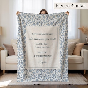 May include: A fleece blanket featuring a blue and white floral pattern border surrounding a central cream-colored panel. The text reads: Never underestimate the difference you made and the lives you've touched. HAPPY RETIREMENT Taylor.