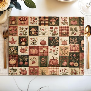 May include: A rectangular placemat featuring a grid of squares with autumn-themed illustrations including various mushrooms, pumpkins, wildflowers, and foliage in shades of orange, brown, green, and cream, set on a white table with gold cutlery.