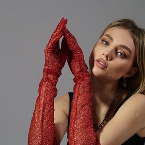 May include: A woman wearing red sparkly gloves poses with a silver disco ball. She is wearing a black tank top and a black and white polka dot skirt.