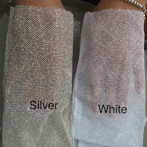 May include: Two pieces of sheer, fine-mesh fabric with a metallic, glittery finish. One piece is labeled Silver and has a warm, reflective tone, while the other is labeled White and features a bright, cool-toned, shimmering appearance.