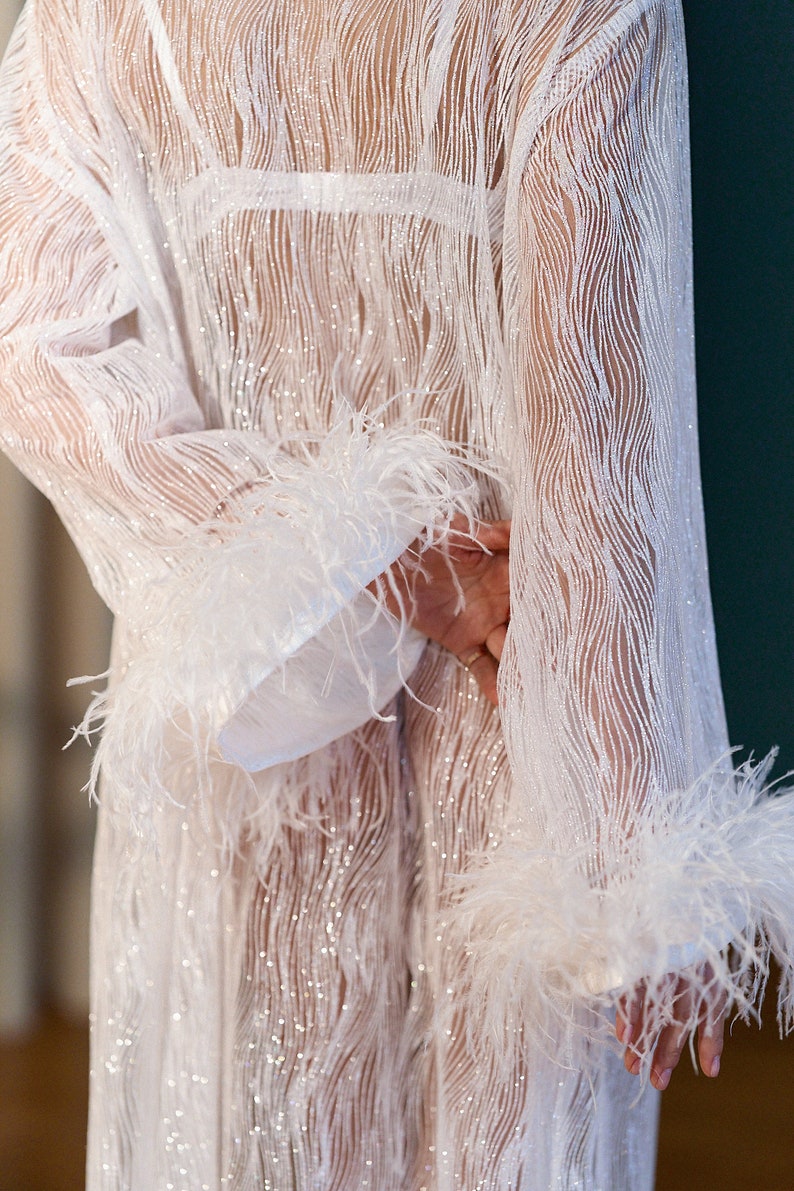 May include: A white sheer robe with a sparkly, wavy pattern and feather trim on the sleeves.