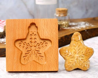 May include: A wooden cookie cutter in the shape of a snowflake star. The cutter is shown next to a baked cookie in the same shape.