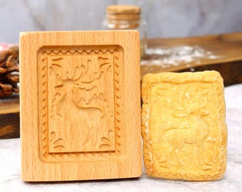 May include: Wooden cookie cutter with a reindeer design. The cutter is next to a cookie with the same design.