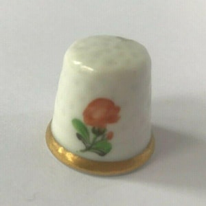 Puede incluir: Dedal de porcelana blanca con borde dorado y una flor naranja pintada a mano con hojas verdes.