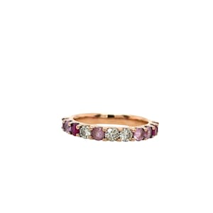May include: Rose gold band ring with alternating pink and clear gemstones. The ring features a series of round-cut pink gemstones and clear gemstones set in a continuous pattern around the band.