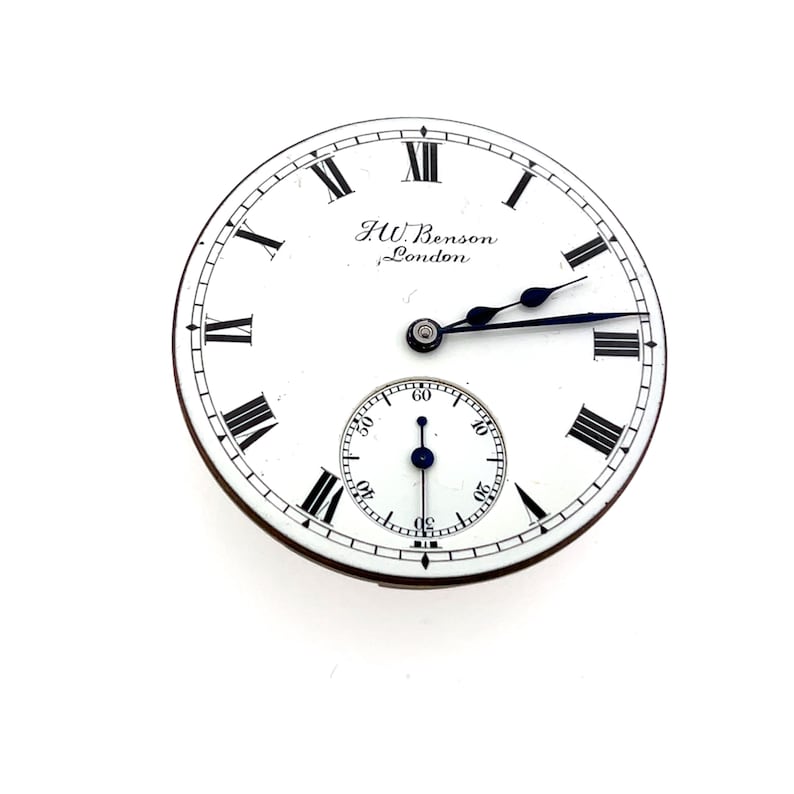 May include: A white pocket watch face with black Roman numerals and hands. The watch face has a smaller subdial at the bottom and the text "J.W. Benson, London" is printed at the top. The watch has a black and silver design.