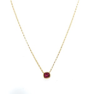 Peut inclure: Un collier à fine chaîne dorée orné d'une unique petite pierre précieuse rouge foncé de taille coussin, sertie dans un chaton en or simple. La chaîne à maillons polis suspend la pierre rouge vive au centre du bijou.