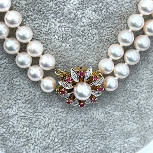 May include: A double strand pearl necklace with a gold clasp featuring a pearl surrounded by diamonds and pink gemstones.