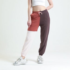 Può includere: Una donna indossa un top corto bianco e pantaloni della tuta a blocchi di colore. I pantaloni della tuta sono divisi in tre sezioni verticali: ruggine, bianco e marrone scuro. L'outfit è completato da scarpe da ginnastica bianche.