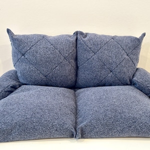 May include: A blue quilted sofa with two large cushions. The sofa is made of a soft, textured fabric.