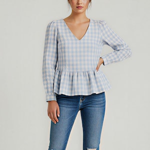 May include: A woman wearing a light blue and white gingham print top with a V-neck and peplum detail. She is wearing blue jeans with distressed knees and brown heeled sandals.