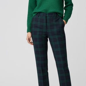 May include: A woman in a green jumper and tartan trousers. The jumper is a solid green, and the trousers have a dark green and navy blue check pattern. The outfit is finished with beige court shoes.
