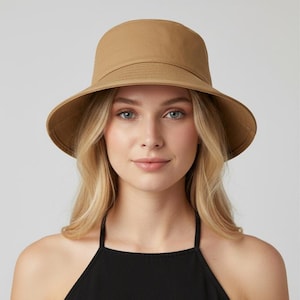 Peut inclure: Un chapeau de type « bucket » de couleur beige avec un large bord. Le chapeau a une couronne structurée et un bord légèrement incliné. Fabriqué dans un tissu robuste, il est conçu pour protéger du soleil. Sa couleur neutre s'accorde avec diverses tenues.