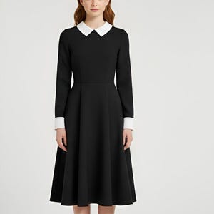 Könnte beinhalten: Ein schwarzes Kleid mit weißem Kragen und Manschetten. Das langärmlige Kleid hat ein figurbetontes Oberteil und einen ausgestellten Rock, der bis zur Mitte der Wade reicht. Das Model trägt schwarze Absätze.