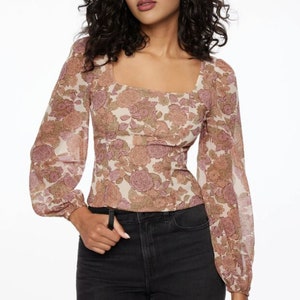 Puede incluir: Una blusa de manga larga con estampado floral y cuello cuadrado. La blusa está hecha de una tela transparente y tiene una silueta ajustada.