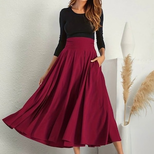 May include: A burgundy high-waisted midi skirt with a flowing, pleated design. The skirt has a fitted waistband and pockets on the sides.
