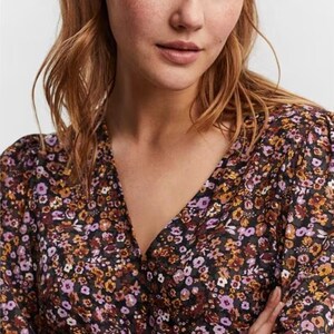 May include: A black floral print blouse with a V-neckline and long sleeves. The blouse has a small, subtle pattern of purple, orange, and white flowers on a black background.