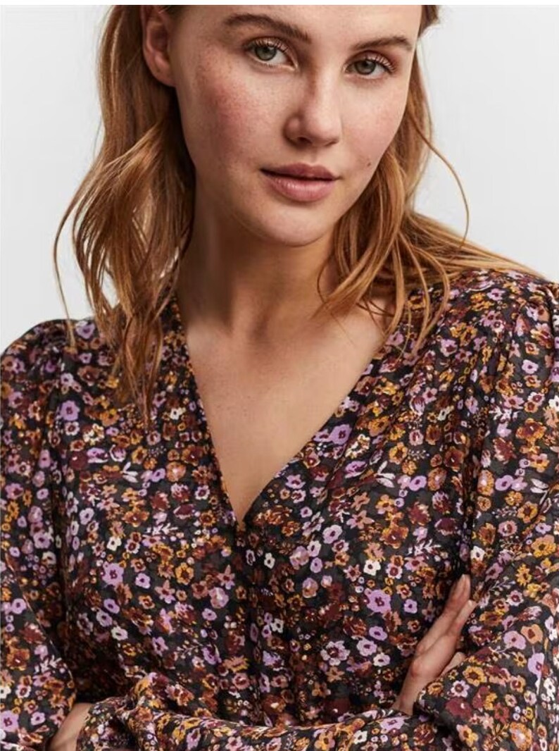 May include: A black floral print blouse with a V-neckline and long sleeves. The blouse has a small, subtle pattern of purple, orange, and white flowers on a black background.