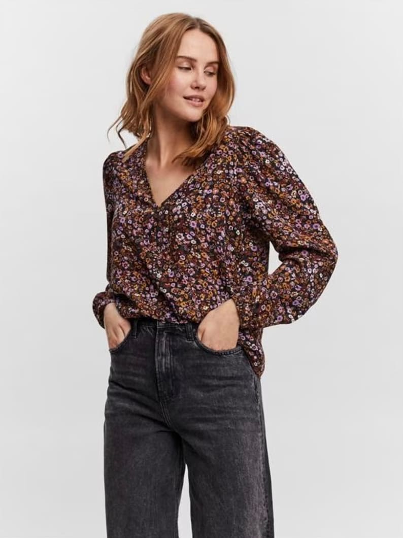 May include: A long-sleeved blouse with a floral print in shades of brown, purple and yellow. The blouse has a V-neckline and a relaxed fit.