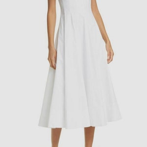 Puede incluir: Un vestido midi blanco sin mangas con escote cuadrado y un corpi&ntilde;o ajustado. El vestido tiene una falda fluida y est&aacute; hecho de una tela ligera.
