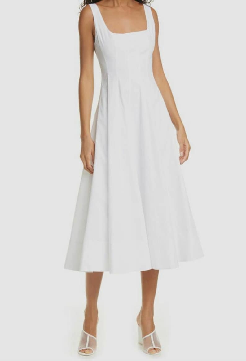 Puede incluir: Un vestido midi blanco sin mangas con escote cuadrado y un corpi&ntilde;o ajustado. El vestido tiene una falda fluida y est&aacute; hecho de una tela ligera.